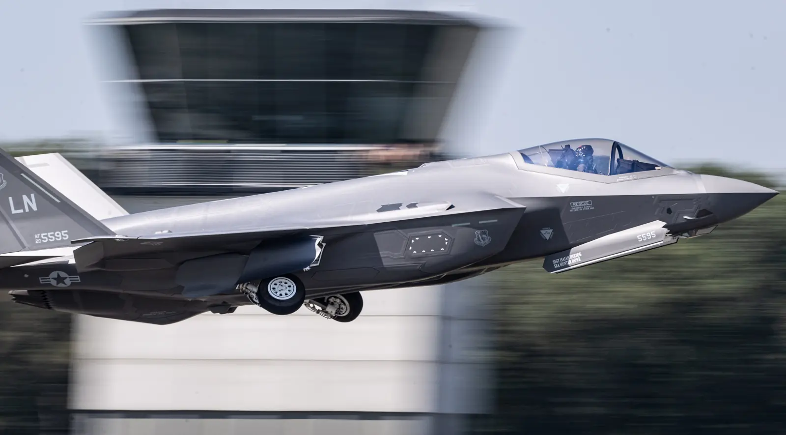 Avion de combat F-35A en vol à basse altitude devant une tour de contrôle